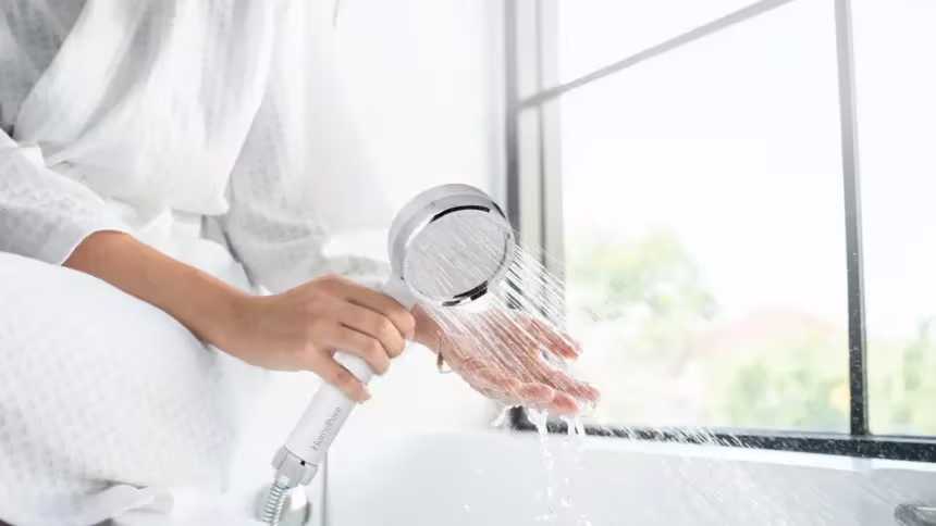 Hand holding a HomePure Rayn shower head with flowing water