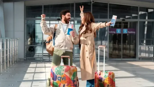 Why Membership Travel Might Be The Smartest Way To Book Your Next Trip 2 couple outside airport cheering with their luggage